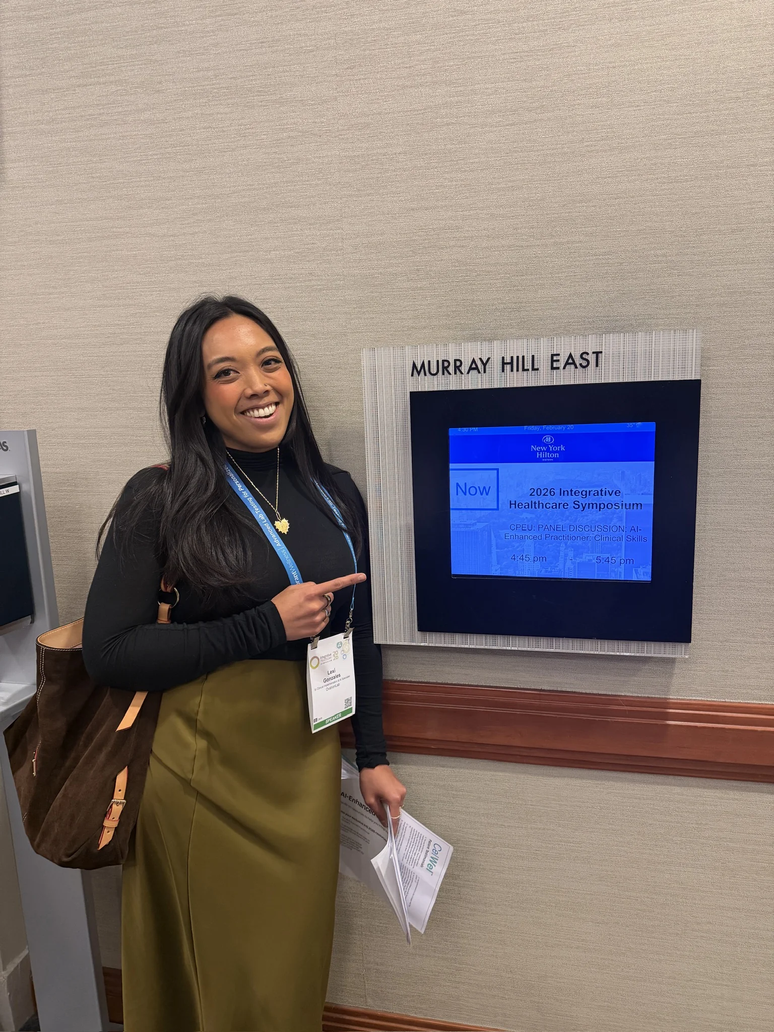 Dr. Lexi Gonzales pointing at the Integrative Healthcare Symposium 2026 session sign